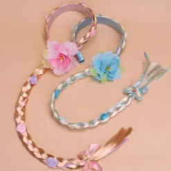 Peruk i prinsessstil med långa flätor och hårband, med en stor flätad blomma i rosa.><noscript><img width=