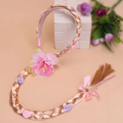 Peruk i prinsessstil med långa flätor och hårband, med en stor flätad blomma i rosa.><noscript><img width=