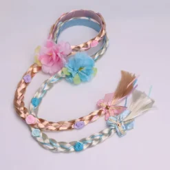 Peruk i prinsessstil med långa flätor och hårband, med en stor flätad blomma i rosa.><noscript><img width=
